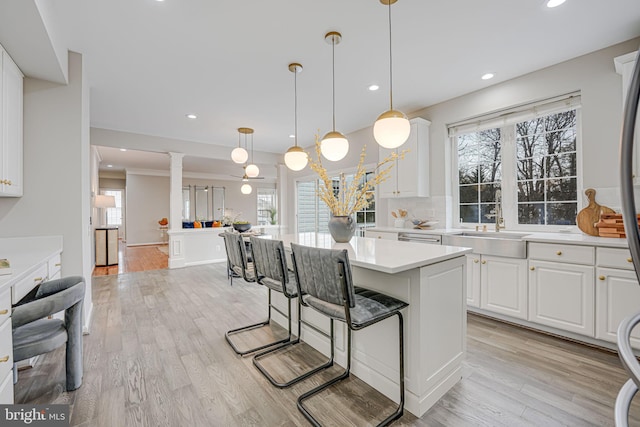 kitchen featuring sink, white cabinetry, a center island, hanging light fixtures, and light hardwood / wood-style flooring