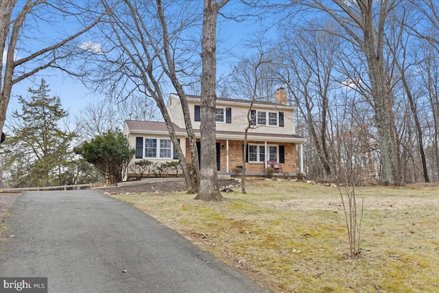 view of front of house featuring driveway, a chimney, covered porch, a front lawn, and brick siding