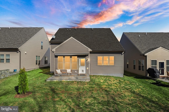 back of property at dusk with a patio area, a shingled roof, and a yard