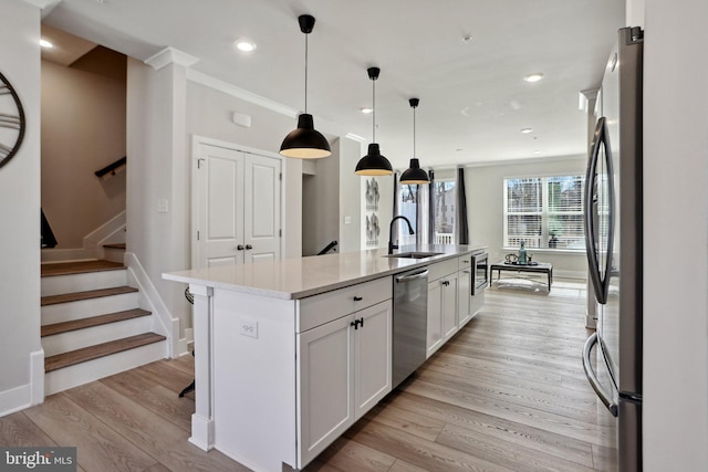 kitchen with stainless steel appliances, light wood-type flooring, white cabinetry, and a kitchen island with sink