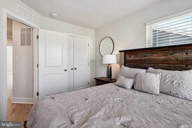 bedroom with baseboards, visible vents, a closet, and wood finished floors