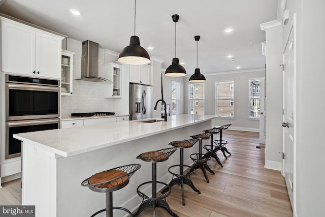 kitchen with stainless steel appliances, white cabinetry, ornamental molding, wall chimney range hood, and tasteful backsplash