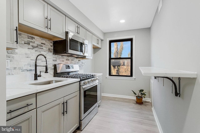 kitchen with a sink, baseboards, appliances with stainless steel finishes, decorative backsplash, and light stone countertops