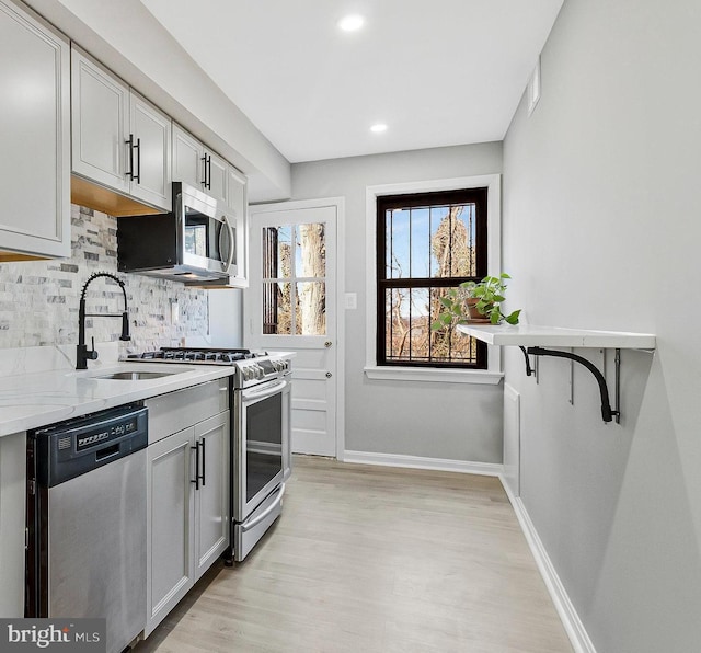 kitchen featuring baseboards, light wood-style flooring, a sink, decorative backsplash, and stainless steel appliances