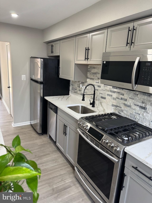 kitchen with light wood-style flooring, a sink, decorative backsplash, gray cabinetry, and stainless steel appliances