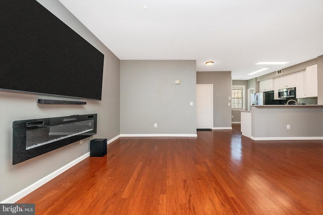 unfurnished living room with a glass covered fireplace, visible vents, baseboards, and wood finished floors