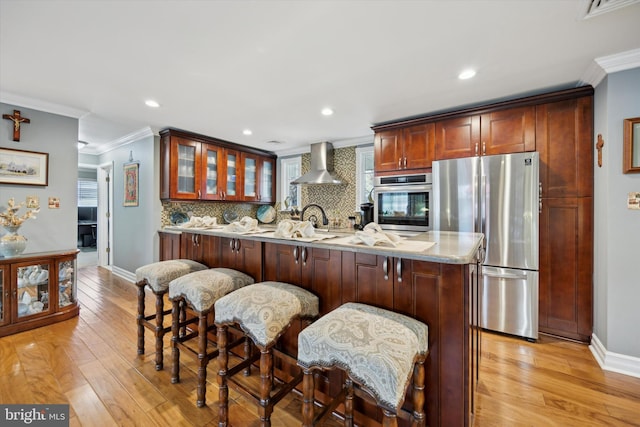 kitchen featuring crown molding, stainless steel appliances, a breakfast bar, and wall chimney exhaust hood