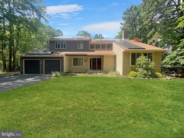 view of front of house with aphalt driveway, a front yard, roof mounted solar panels, and a garage