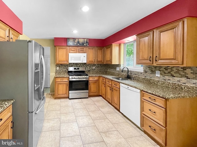 kitchen with stainless steel appliances, a sink, dark stone counters, tasteful backsplash, and brown cabinetry