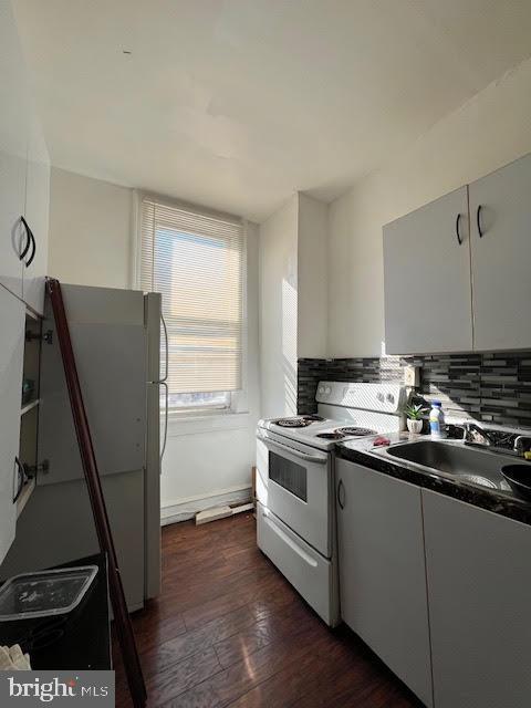 kitchen featuring dark countertops, decorative backsplash, dark wood-type flooring, a sink, and white appliances