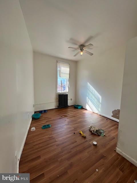 empty room featuring radiator heating unit, baseboards, dark wood finished floors, and a ceiling fan