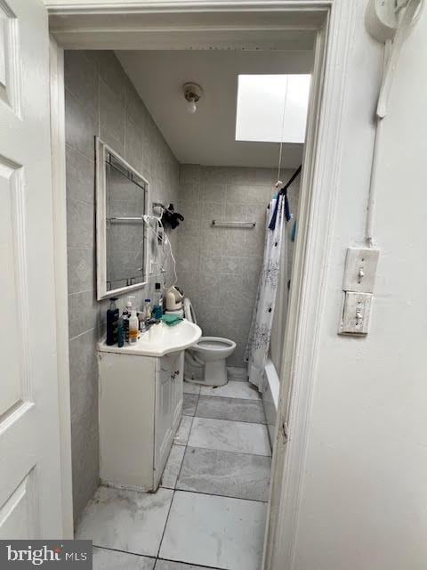 full bath with toilet, a shower with shower curtain, a skylight, and vanity