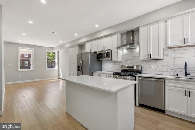 kitchen with stainless steel appliances, sink, wall chimney range hood, and white cabinets