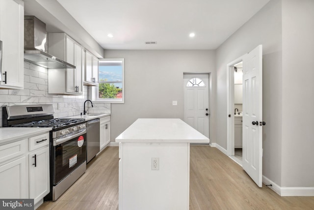 kitchen with white cabinetry, stainless steel appliances, wall chimney exhaust hood, and a kitchen island