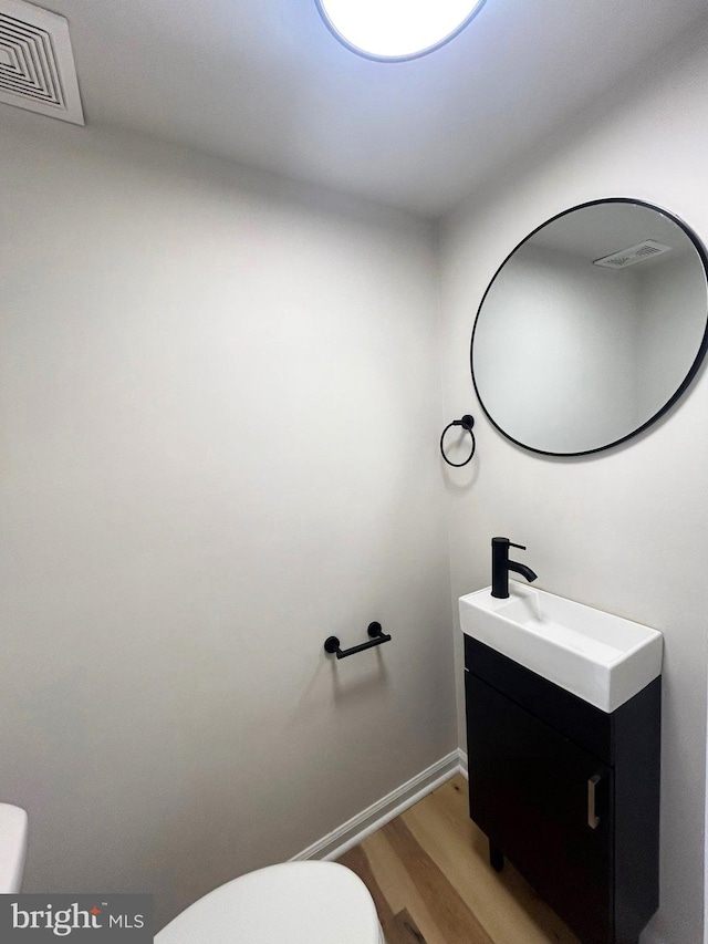 half bathroom featuring toilet, visible vents, wood finished floors, and vanity