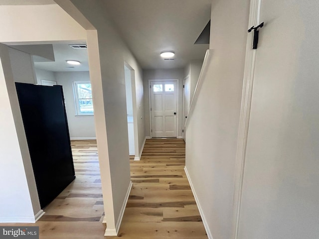 hall with baseboards, visible vents, and light wood-style floors