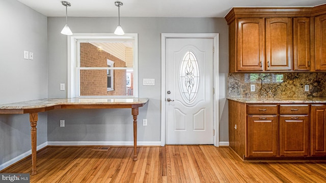 kitchen with decorative light fixtures, light stone counters, light hardwood / wood-style floors, and decorative backsplash