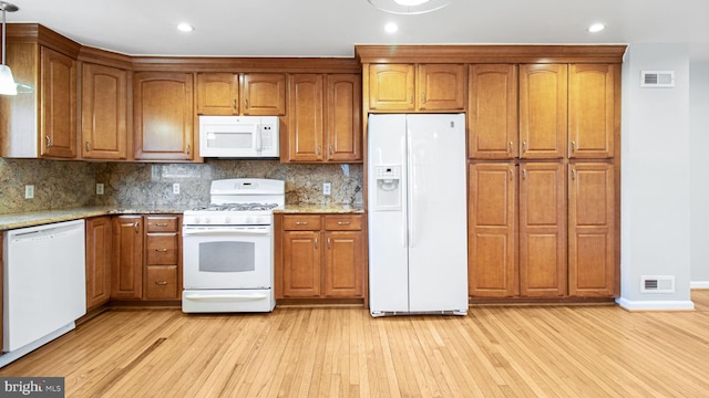 kitchen with white appliances, backsplash, light stone countertops, decorative light fixtures, and light wood-type flooring