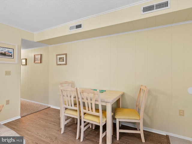 dining area featuring crown molding, wood-type flooring, and a textured ceiling