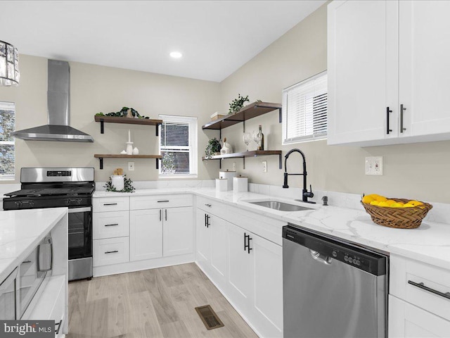 kitchen with white cabinetry, sink, light stone counters, stainless steel appliances, and wall chimney range hood