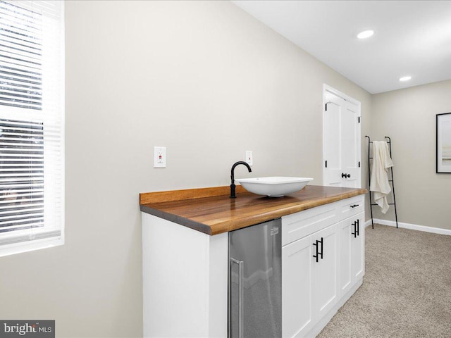 bar featuring sink, wooden counters, stainless steel refrigerator, white cabinetry, and light carpet