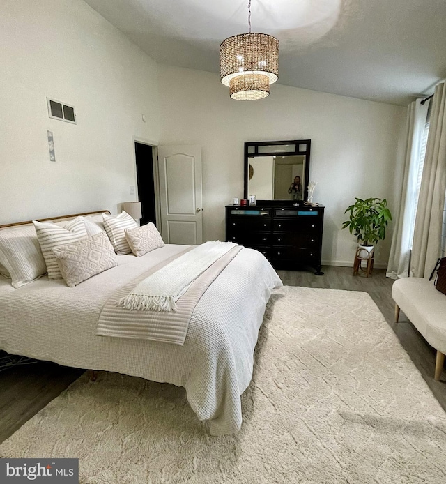 bedroom featuring vaulted ceiling, hardwood / wood-style floors, and a notable chandelier