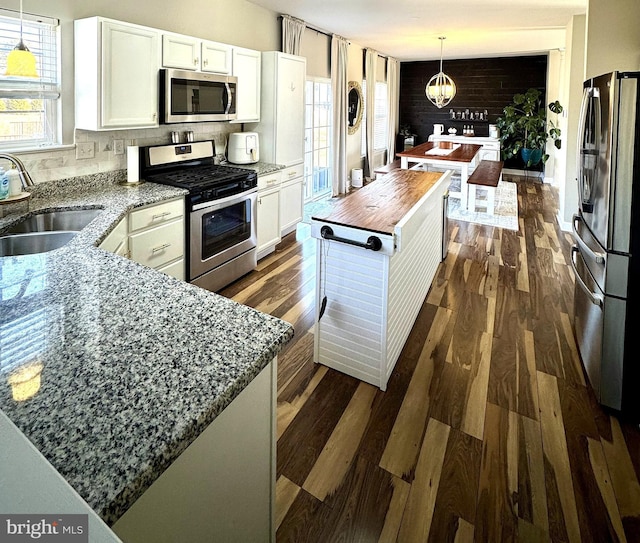 kitchen with sink, white cabinets, decorative backsplash, hanging light fixtures, and stainless steel appliances