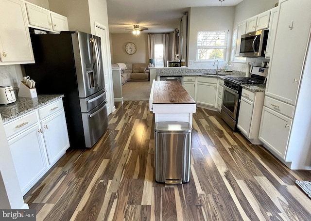 kitchen with appliances with stainless steel finishes, butcher block counters, sink, white cabinets, and dark wood-type flooring