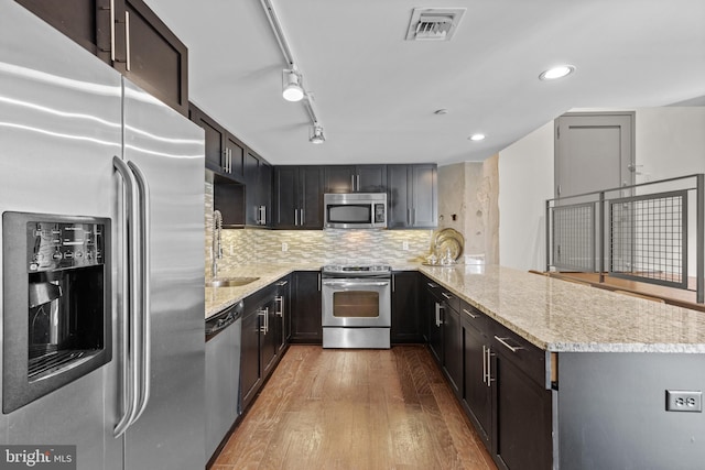 kitchen with sink, tasteful backsplash, wood-type flooring, kitchen peninsula, and stainless steel appliances