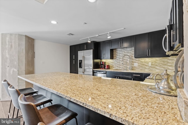 kitchen with sink, appliances with stainless steel finishes, a kitchen breakfast bar, kitchen peninsula, and decorative backsplash