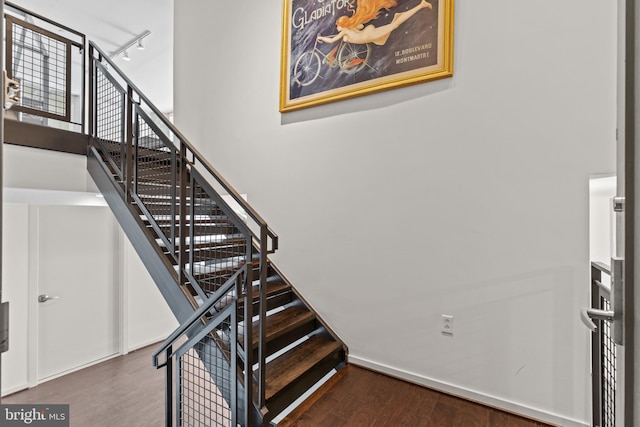 staircase featuring hardwood / wood-style flooring, rail lighting, and a towering ceiling