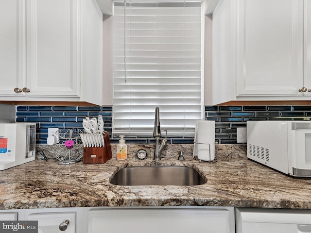 kitchen with white microwave, a sink, and white cabinetry