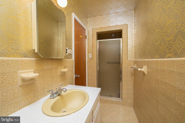 bathroom with a shower with door, vanity, and tile walls