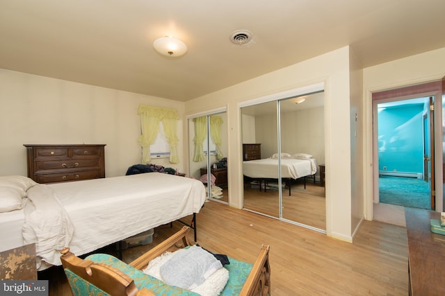 bedroom featuring a baseboard heating unit, multiple closets, and light wood-type flooring