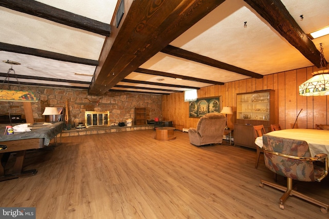 living room with a stone fireplace, wood walls, beamed ceiling, and hardwood / wood-style flooring