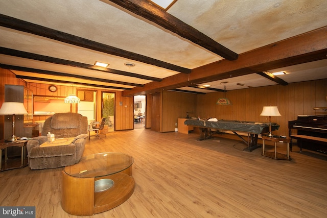 playroom featuring beamed ceiling, wooden walls, a textured ceiling, and light hardwood / wood-style floors