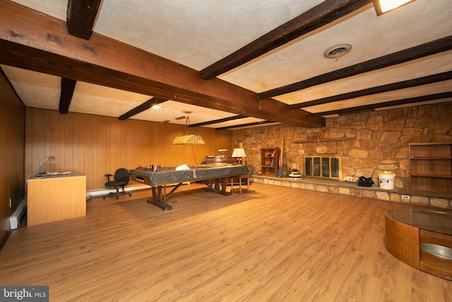 playroom featuring a stone fireplace, light hardwood / wood-style floors, and a textured ceiling