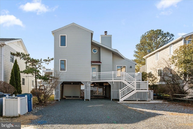 back of house featuring a chimney, a carport, driveway, a wooden deck, and stairs