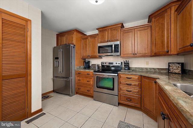 kitchen with brown cabinets, stainless steel appliances, visible vents, light tile patterned flooring, and baseboards