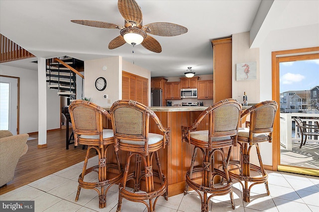 kitchen with brown cabinetry, stainless steel microwave, a breakfast bar area, refrigerator, and light countertops