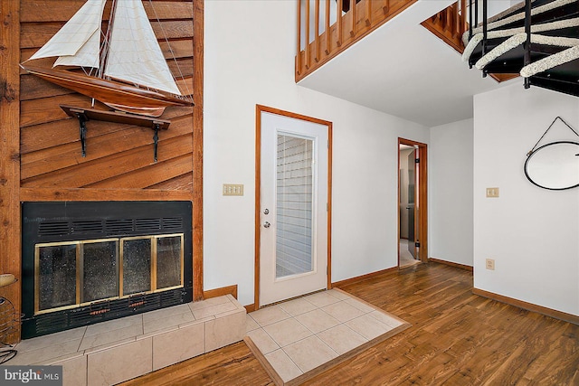 foyer entrance featuring wood finished floors, a glass covered fireplace, a towering ceiling, and baseboards