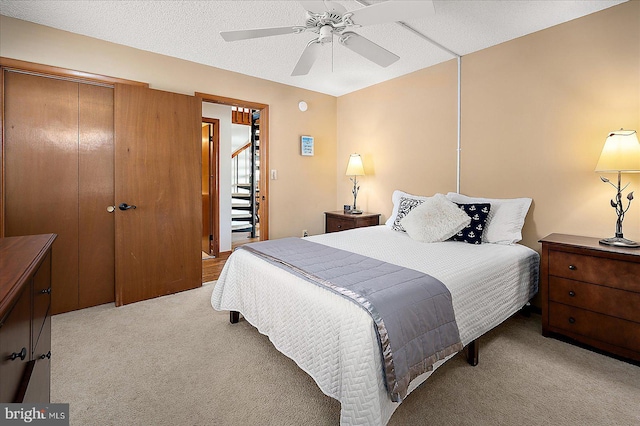 bedroom with a closet, light colored carpet, ceiling fan, and a textured ceiling