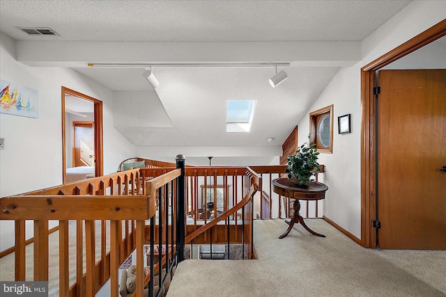 hallway featuring a textured ceiling, a skylight, an upstairs landing, carpet, and track lighting