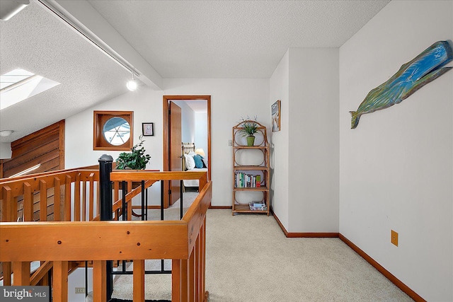 corridor with carpet, lofted ceiling with skylight, a textured ceiling, an upstairs landing, and baseboards