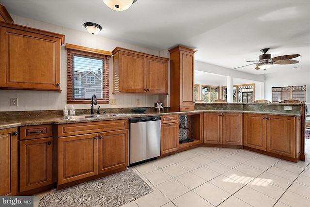 kitchen featuring dark countertops, brown cabinets, a healthy amount of sunlight, stainless steel dishwasher, and a sink