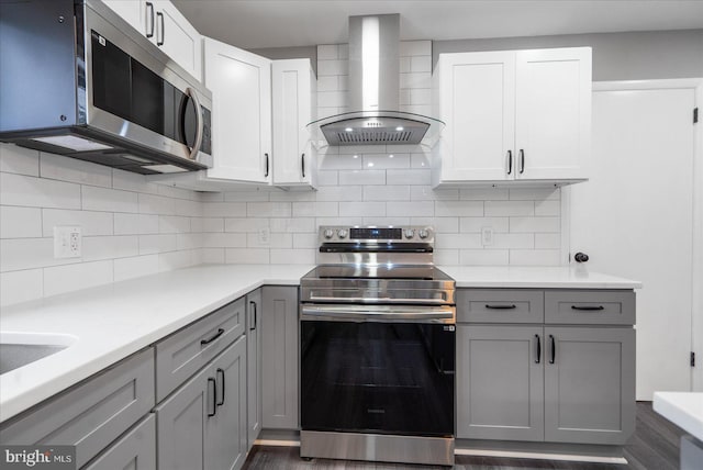 kitchen featuring appliances with stainless steel finishes, white cabinetry, gray cabinetry, backsplash, and wall chimney exhaust hood