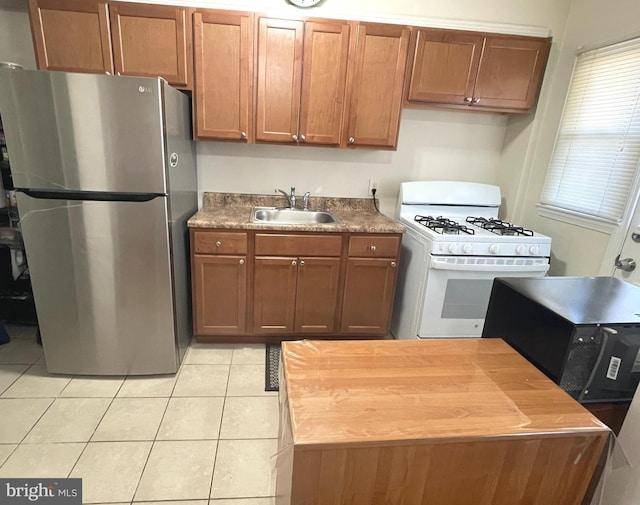 kitchen featuring stainless steel fridge, sink, white range with gas stovetop, and light tile patterned floors