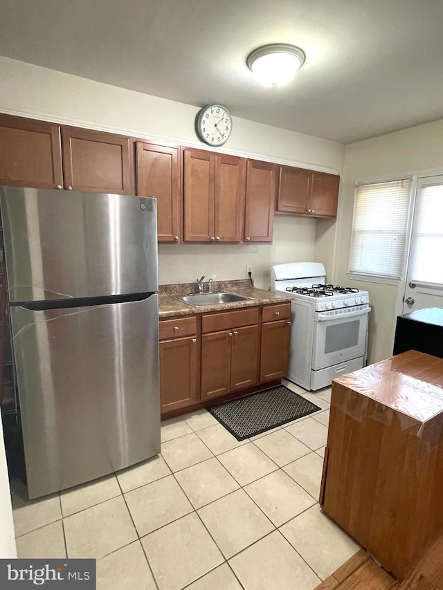 kitchen featuring white gas range oven, sink, stainless steel refrigerator, and light tile patterned flooring