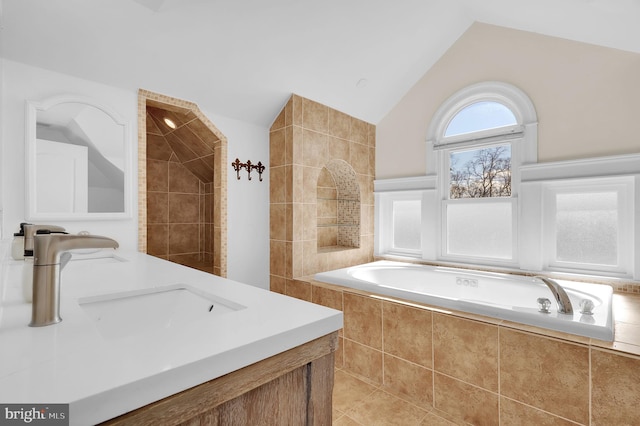 bathroom featuring tiled tub, vaulted ceiling, and vanity