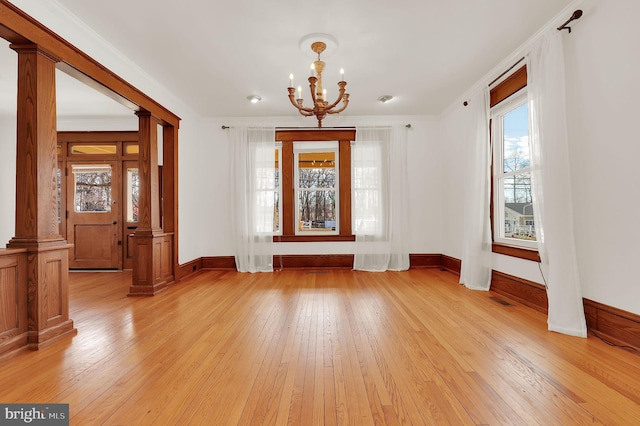 spare room featuring light wood-type flooring, ornamental molding, ornate columns, and a chandelier